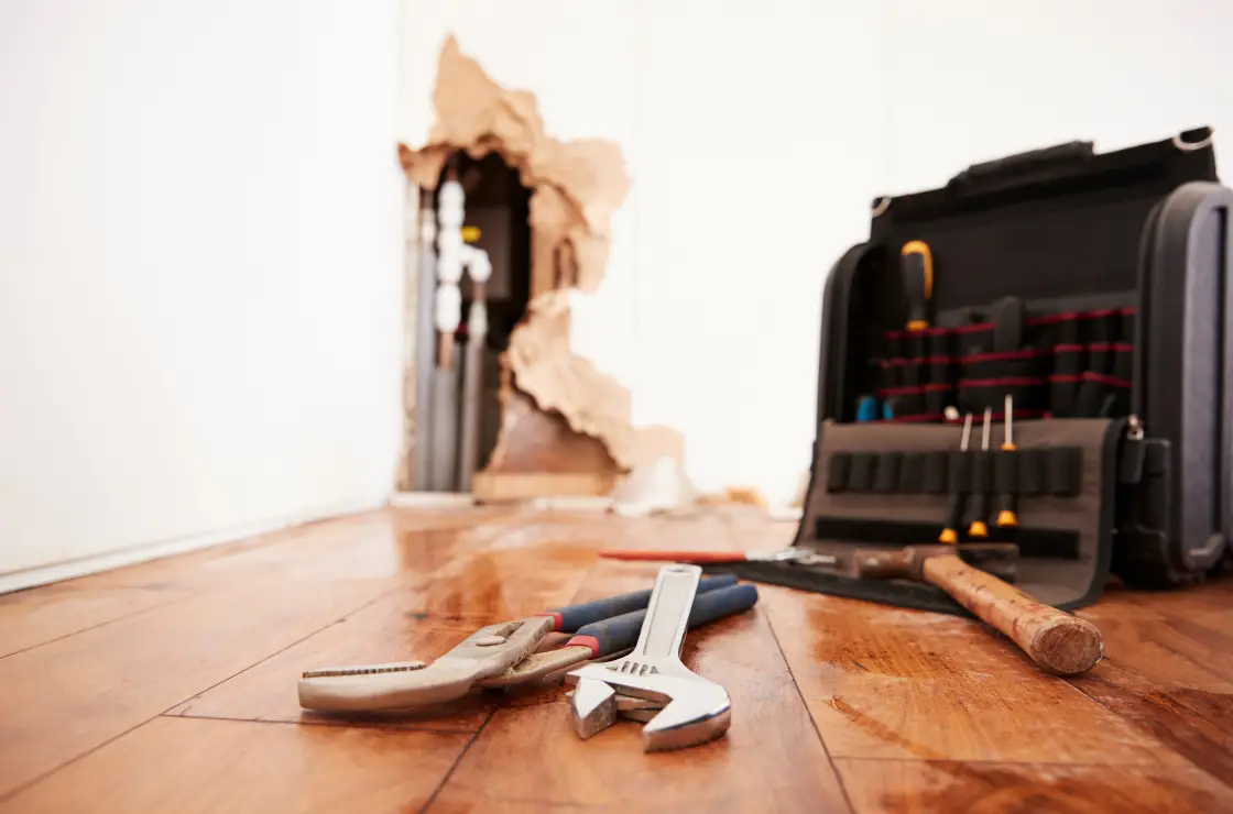 water damage prevention tips for flooring - repair tools in front on a wet wood floor with exposed plumbing in the background